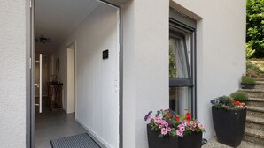 A modern building entrance with a sliding door, a small table with shoes, and two large flower planters. - Apartment 'Ferienwohnung' with Private Terrace, Private Garden and Wi-Fi (Sinsheim)