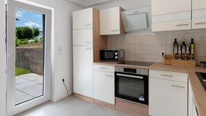 A modern kitchen with white cabinets, a microwave, an oven, and a view of the outdoors. - Apartment 'Ferienwohnung' with Private Terrace, Private Garden and Wi-Fi (Sinsheim)