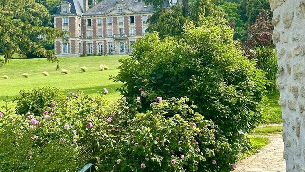 Un edificio grande e histórico con un césped bien cuidado y flores en floración en primer plano.