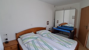 Une chambre à coucher avec un lit, une table de chevet en bois, une commode, un miroir et une porte.
