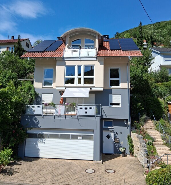 Une maison à deux étages avec un garage, un balcon et des panneaux solaires sur le toit.