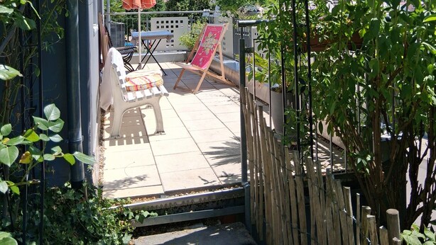 Un espace extérieur aménagé en terrasse, avec une table et des chaises, une clôture en bois et une vue sur les montagnes en arrière-plan.
