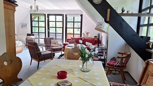 Una habitación con una cama, una mesa de comedor con mantel de lunares, un cuenco rojo y un jarrón con flores.