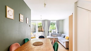 A dining area with a wooden table and chairs, a sofa, and a view of the outdoors through large windows. - Stylish Islington Garden Flat Sleeps Four (London)