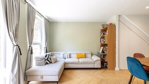 A modern living room with a sectional sofa, a wooden bookshelf, and a dining area. - Stylish Islington Garden Flat Sleeps Four (London)