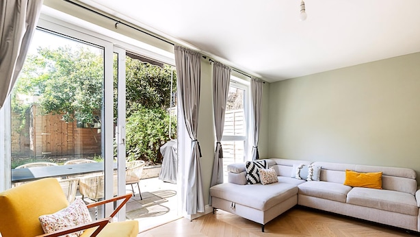 A modern living room with a sofa, a yellow armchair, and a glass door leading to an outdoor patio. - Stylish Islington Garden Flat Sleeps Four (London)
