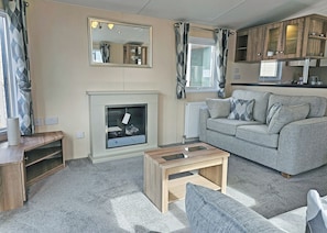 A living room with a fireplace, a sofa, a coffee table, and wooden cabinets. - Smart, modern two bedroom caravan, perfect for couples and families alike. (Aldbrough)