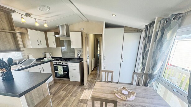 A compact kitchen with a central island, a dining table with chairs, and a view through a window. - Smart, modern two bedroom caravan, perfect for couples and families alike. (Aldbrough)