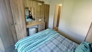 A bedroom with a bed, a wardrobe, a mirror, and a desk. - Smart, modern two bedroom caravan, perfect for couples and families alike. (Aldbrough)