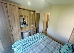 A bedroom with a bed, a wardrobe, a mirror, and a desk. - Smart, modern two bedroom caravan, perfect for couples and families alike. (Aldbrough)