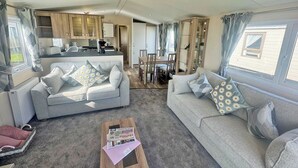A compact living space with a kitchenette, two sofas with patterned cushions, a dining table, and a small coffee table. - Smart, modern two bedroom caravan, perfect for couples and families alike. (Aldbrough)