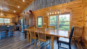 A wooden cabin interior with a dining area, kitchen, and large windows. - Evergreen Echo | Cabin w/ Mountain Views, Theater, Game Room, and Hot Tub (Gatlinburg)