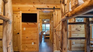 A wooden interior with a hallway leading to a bedroom with a bed and a window. - Evergreen Echo | Cabin w/ Mountain Views, Theater, Game Room, and Hot Tub (Gatlinburg)