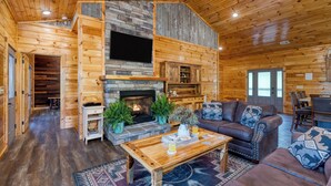 A log cabin interior with a stone fireplace, wooden walls, a sofa, and a coffee table. - Evergreen Echo | Cabin w/ Mountain Views, Theater, Game Room, and Hot Tub (Gatlinburg)