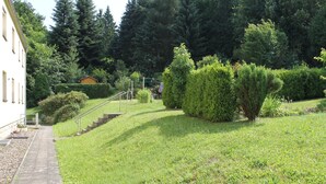 A grassy area with a pathway leading to a building, surrounded by trees and bushes. - Vacation apartment Zum Vierbeiner (Pirna)