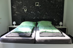 A double bed with green and black bedding, two bedside tables with lamps, and a dark textured wall with two small framed pictures.