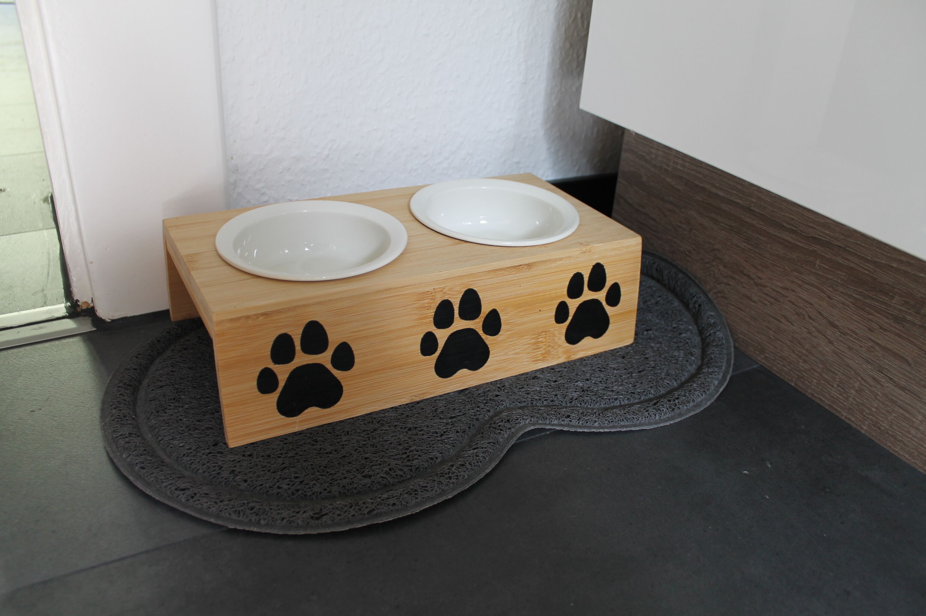 Un distributeur de nourriture pour animaux de compagnie en bois, doté de deux gamelles posées sur un tapis foncé.