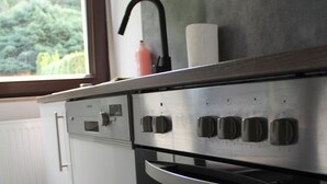 A kitchen with a built-in oven, a window with a view of greenery, and a white cabinet. - Vacation apartment Zum Vierbeiner (Pirna)