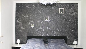 A bedroom with a dark textured headboard, two bedside tables with lamps, a bed with a leaf-patterned duvet, and three small framed pictures on the headboard. - Vacation apartment Zum Vierbeiner (Pirna)
