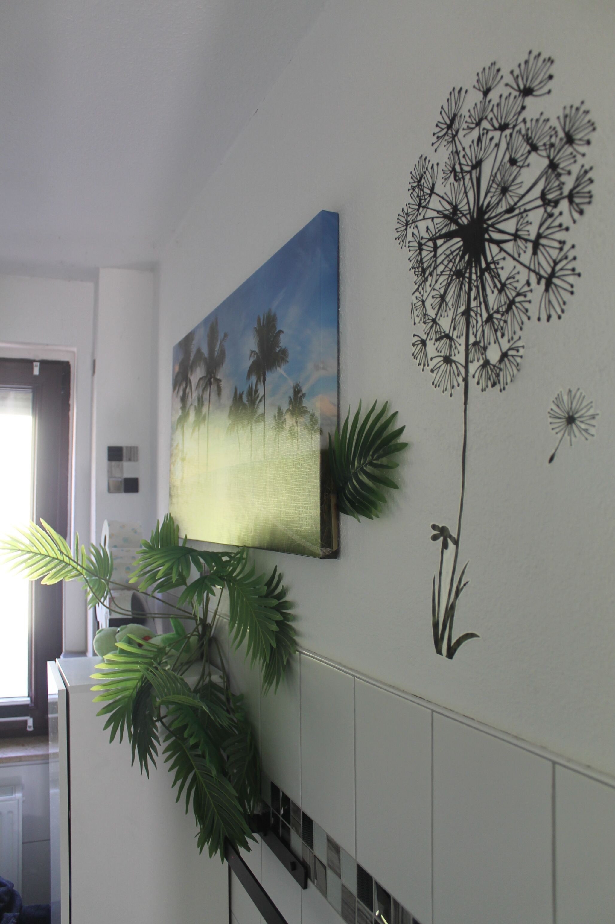 A wall with a painting of palm trees, a dandelion, and a potted plant.