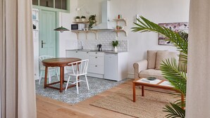 Cocina compacta con armarios blancos, una puerta verde y un comedor con mesa de madera y sillas blancas.