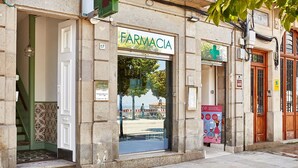 Una farmacia con un amplio ventanal, un letrero con una cruz verde e indicación de que es farmacia.