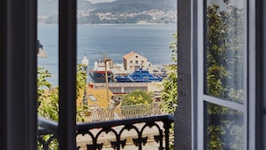Vista costera desde una ventana con vista a un puerto con barcos, un edificio con 'ADUANAS' en el techo y un telón de fondo montañoso.