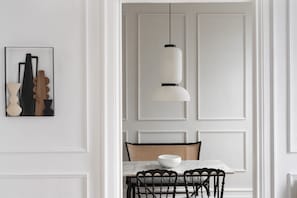 A dining area with a white table, black chairs, a woven chair, a hanging light fixture, and a framed artwork on the wall. - Suite By Olivo (Vigo)