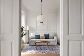 A white room with a sofa, a coffee table, and a hanging light fixture. - Suite By Olivo (Vigo)