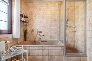 Une salle de bain équipée d’une baignoire, d’une douche et d’un espace de douche séparé par des parois en verre.