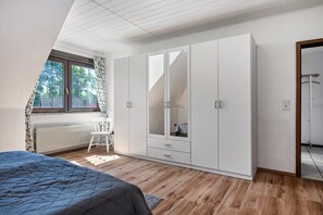 Une chambre à coucher comprenant un lit, une armoire, un radiateur, une fenêtre avec des rideaux et une vue sur l’extérieur.