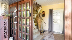 A wooden front door with glass panels, a staircase with a wrought iron railing, and a welcome sign. - Apartment 'Storchenallee' (Burg (Dithmarschen))