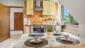 A modern kitchen with wooden cabinets, a gas stove, and a dining area with a table set for four. - Apartment 'Storchenallee' (Burg (Dithmarschen))