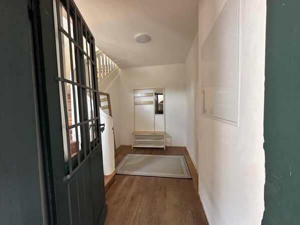 Un pasillo con suelo de madera, un perchero blanco y una puerta negra con paneles de vidrio.