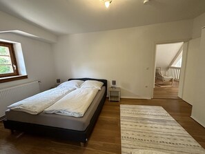 Un dormitorio con cama, mesitas de noche, una ventana y vistas a un balcón exterior.