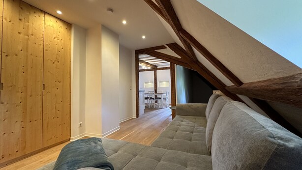 Une pièce de style « loft », avec un plafond haut, des poutres apparentes, un canapé et un coin repas à l’arrière-plan.