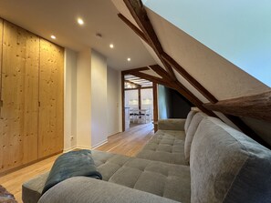 Ein Loft-Zimmer mit hohen Decken, freiliegenden Holzbalken, einer Couch und einem Essbereich im Hintergrund.