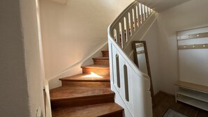 Un escalier avec des marches en bois et des rampes blanches, menant à un palier agrémenté d’un miroir et d’une étagère.