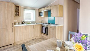 A modern kitchen with wooden cabinets, a microwave, a stove, and a window with blinds.