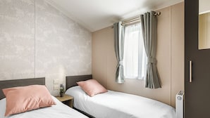 A hotel room with two beds, a window with curtains, a radiator, and a wall with a tree pattern.