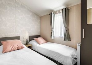 A hotel room with two beds, a window with curtains, a radiator, and a wall with a tree pattern.