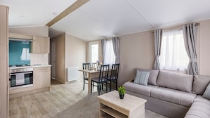 A modern living room with a sofa, a coffee table, a dining area with chairs, and a kitchen with an oven.