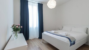 Ein modernes Schlafzimmer mit einem großen Bett, einem Nachttisch, einer Vase mit Blumen und einem Fenster mit Vorhängen.