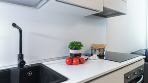 Eine moderne Küche mit einem schwarzen Spülbecken, einem Topf Basilikum, frischen Tomaten und einer Nudelschüssel Spaghetti.