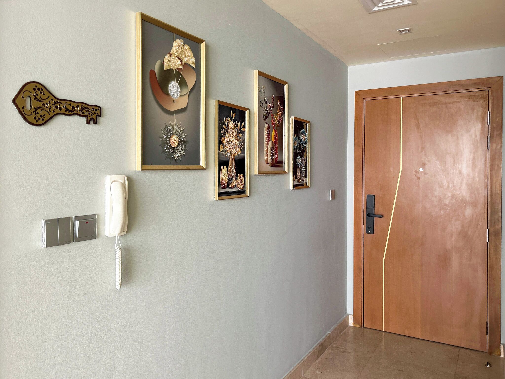 A hallway with a wooden door, a wall-mounted telephone, and three framed artworks.