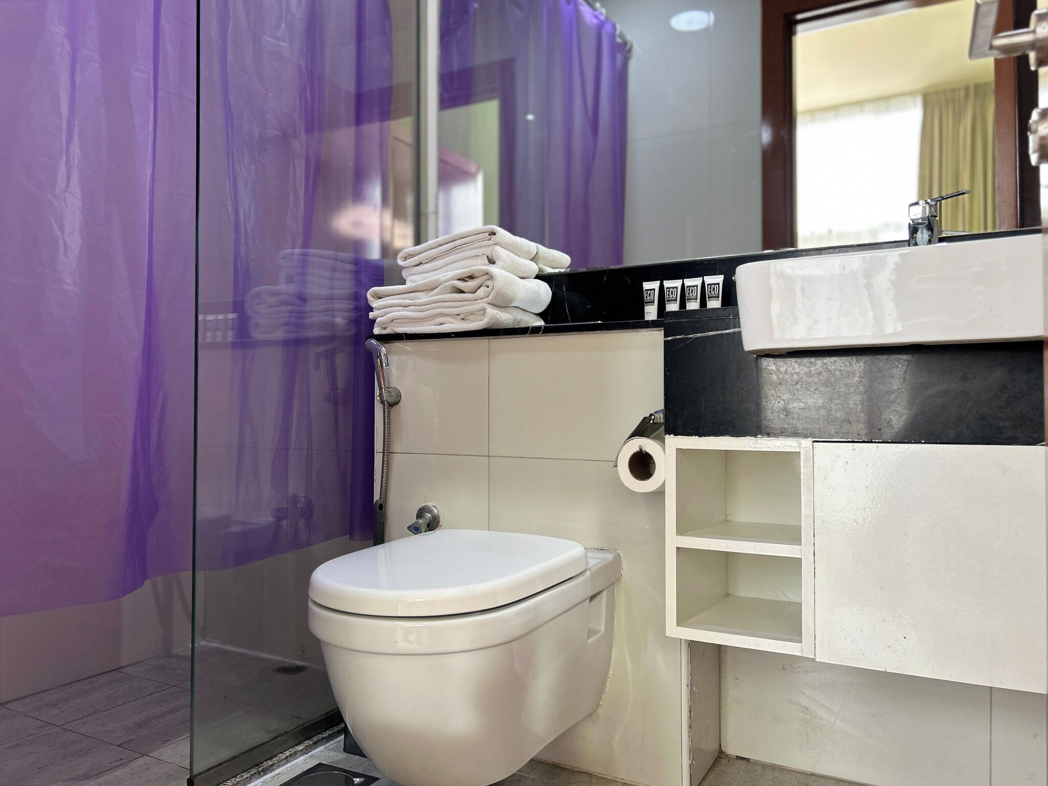 Une salle de bain avec des toilettes blanches, une douche en verre et un lavabo doté d’un plan de travail noir.