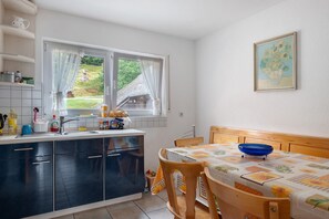 A kitchen with a window, a dining table with a blue bowl, and a painting on the wall. - Apartment 'Faller' with Mountain View, Private Garden and Wi-Fi (Stegen)