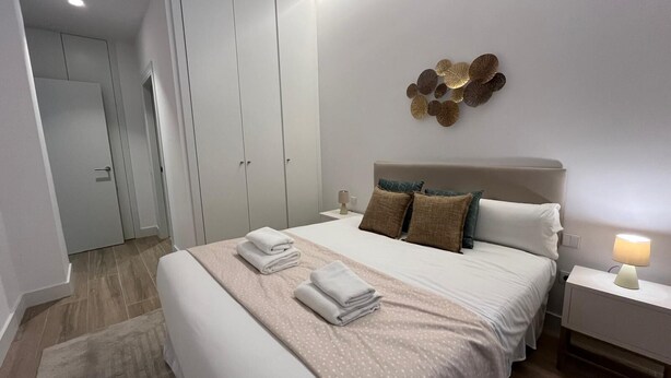 Une chambre d’hôtel moderne, dotée d’un grand lit, d’une table de chevet, d’un élément décoratif fixé au mur et d’une armoire.