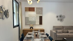 Un espace de repas moderne avec une table en bois dressée pour six personnes, une peinture abstraite contemporaine et un canapé aux lignes épurées en arrière-plan.