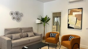 Un salon moderne comprenant un canapé, deux fauteuils, une table basse, un lampadaire, une plante en pot et une œuvre d’art abstraite.
